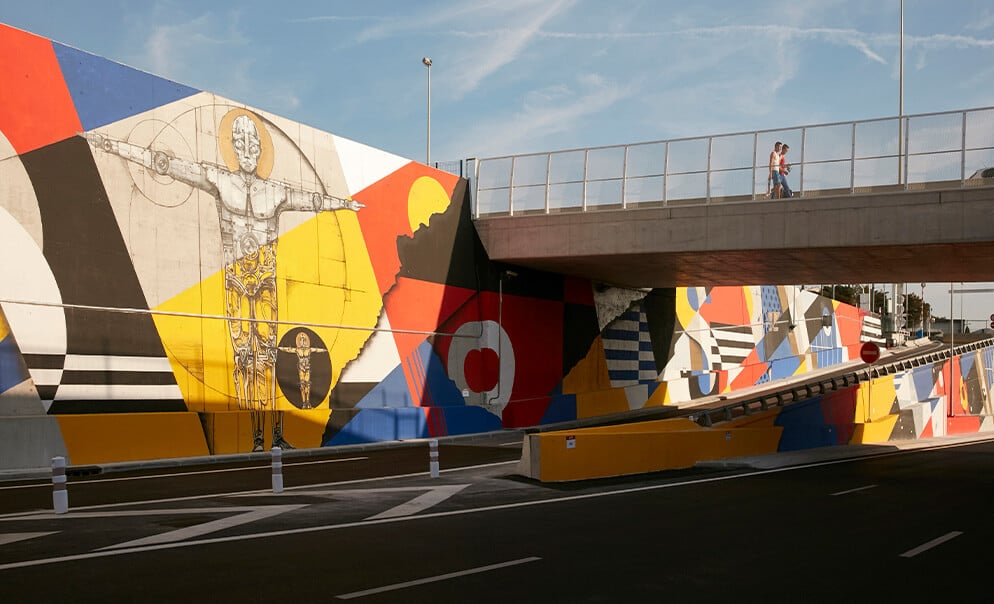 People walking over bridge overlooking graffiti